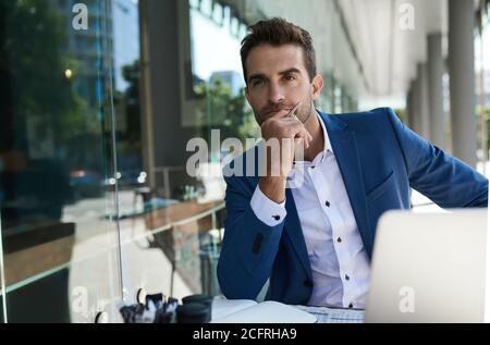 Junger Geschäftsmann, der über die Arbeit an einem Café-Tisch nachdenkt Stockfoto