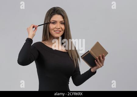 latina Frau mit langen Haaren Mascara auf ihre Wimpern, in der anderen Hand hält sie einen Spiegel, trägt einen schwarzen Jumpsuit, Studio Stockfoto