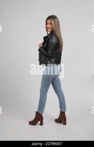 Nette Frau in Lederjacke und jean, stehend zeigt ihren Rücken auf einem grauen Hintergrund, Studio Stockfoto