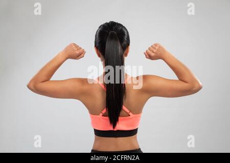 Junge Frau macht Übung, stehen nach hinten mit rosa oben und Frisur, Studio mit grauem Hintergrund Stockfoto