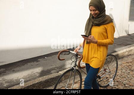 Frau in Hijab mit Smartphone beim Gehen mit dem Fahrrad Stockfoto