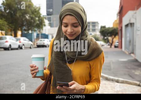 Frau in Hijab mit Kaffeetasse mit Smartphone auf dem Straße Stockfoto