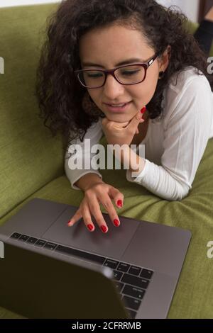 Lockige Frau, die auf einem grünen Sofa in einer Arbeit liegt Beleuchtetes Büro Stockfoto