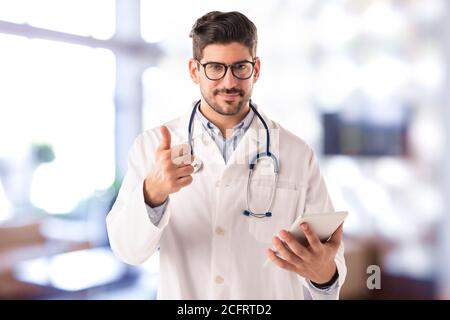 Porträtaufnahme eines männlichen Arztes, der Daumen hoch gibt und ein digitales Tablet benutzt, während er im Krankenhaus steht. Stockfoto