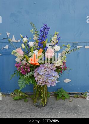 Elegante Blumenarrangements vor einem rustikalen urbanen Hintergrund. Hortensien, Lerkspur, Rosen, Lilien, etc. In einer klaren Glasvase. Stockfoto