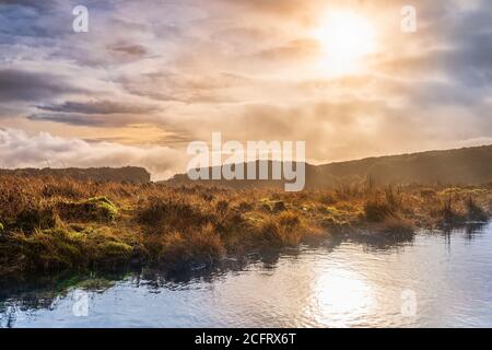 Nebel, Nebel und dramatischer Himmel über einem Sumpf oder Moor mit Sonne, die in einem See reflektiert. Dramatische Landschaft der Wicklow Berge, Irland Stockfoto