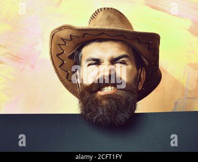 Bärtiger Mann, langer Bart. Brutal kaukasisch lustig unrasiert Hipster in vintage Cowboy Hut mit blauem Papier Blatt im Studio auf bunten Hintergrund Stockfoto