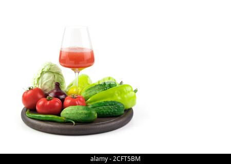 Ein Glas frisch gepresster Gemüsesaft und frisches Gemüse auf einem runden Tablett auf weißem Hintergrund. Stockfoto
