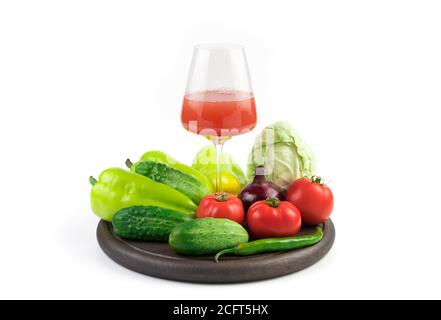Eine große Auswahl an Gemüse und ein Glas frisch gepresster Gemüsesaft auf einem runden Tablett auf weißem Hintergrund. Stockfoto