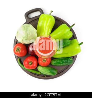 Eine große Auswahl an Gemüse und ein Glas frisch gepresster Gemüsesaft auf einem runden Tablett auf weißem Hintergrund. Stockfoto