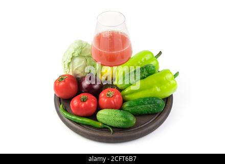 Eine große Auswahl an Gemüse und ein Glas frisch gepresster Gemüsesaft auf einem runden Tablett auf weißem Hintergrund. Stockfoto