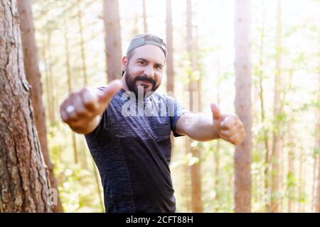 Wanderer im Buchenwald hebt den Daumen im Sieg. Natürliches Licht filtert durch die Äste. Stockfoto