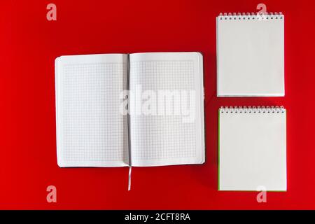 Minimalistisches Layout für Design. Bürobedarf - Notizbücher und Stifte auf rotem Hintergrund. Öffnen Sie ein leeres Notizbuch für Ihre Notizen auf rotem Hintergrund Stockfoto