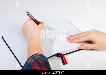 Die junge Frau hält einen Stift in der linken Hand und schreibt eine Notiz in ein leeres Notizbuch. Internationaler Tag Der Linken Stockfoto