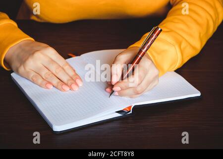 Die junge Frau hält einen Stift in der linken Hand und schreibt eine Notiz in ein leeres Notizbuch. Internationaler Tag Der Linken Stockfoto