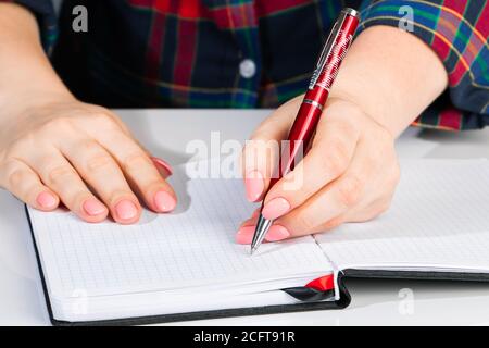 Die junge Frau hält einen Stift in der linken Hand und schreibt eine Notiz in ein leeres Notizbuch. Internationaler Tag Der Linken Stockfoto