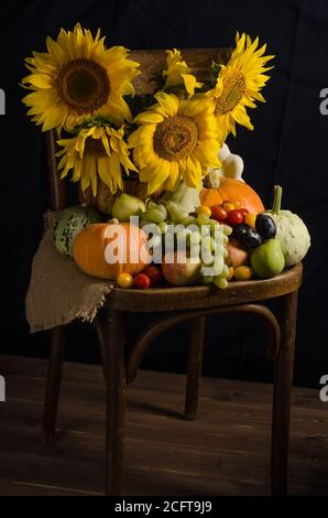 Stillleben mit Sonnenblumen aus Gemüse und Obst auf schwarzem Hintergrund im dunklen Stil. Erntedankfest und Ernte. Stockfoto