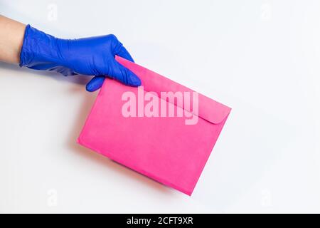 Ein Mann in medizinischen Latexhandschuhen liefert einen Umschlag auf weißem Hintergrund. Das Konzept der sicheren Lieferung von Waren während der Coronavirus-Pandemie. Stockfoto