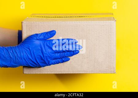 Ein Mann in medizinischen Latexhandschuhen liefert ein Paket auf gelbem Hintergrund. Das Konzept der sicheren Lieferung von Waren während der Coronavirus-Pandemie. Stockfoto
