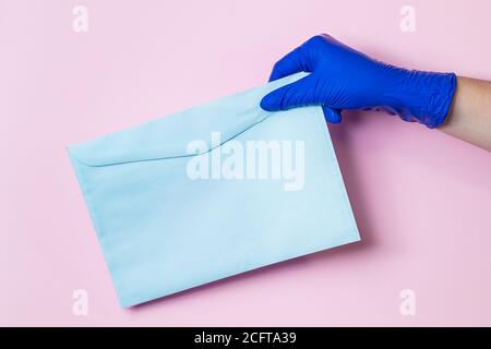 Ein Mann in medizinischen Latexhandschuhen liefert einen Umschlag auf einem rosa Hintergrund. Das Konzept der sicheren Lieferung von Waren während der Coronavirus-Pandemie. Stockfoto