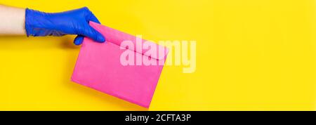 Ein Mann in medizinischen Latexhandschuhen liefert einen Umschlag auf gelbem Hintergrund. Das Konzept der sicheren Lieferung von Waren während der Coronavirus-Pandemie. Stockfoto