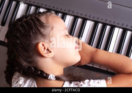 Baby-Mädchen in weißem Kleid schlafen auf Tasten des elektronischen Klaviers, Synthesizer, Nahaufnahme Stockfoto