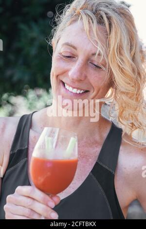 Junge reife blonde Frau in Sportswear Outdoor mit einem Glas Tomatensaft. Stockfoto