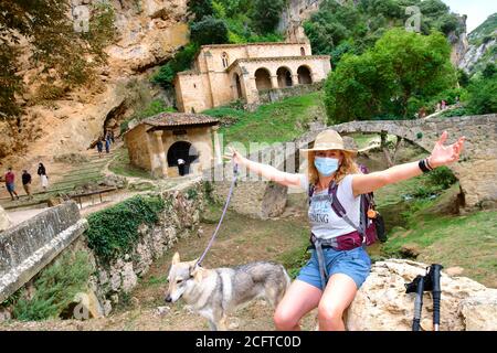 Wanderer reife junge Frau mit einer Gesichtsmaske und einem Hund in der Nähe einer alten Kapelle. Stockfoto