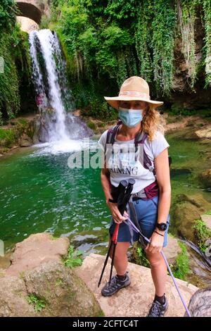 Wanderer reife junge Frau mit einer Gesichtsmaske und Wasserfall. Stockfoto