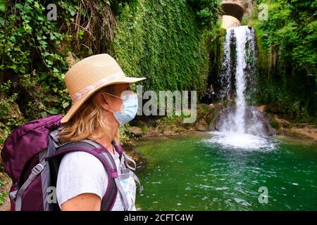 Wanderer reife junge Frau mit einer Gesichtsmaske und Wasserfall. Stockfoto