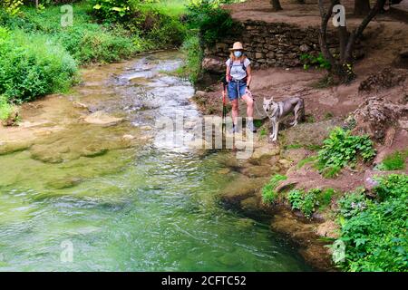 Wanderer reife junge Frau mit einer Gesichtsmaske und ein Hund in einem Flussufer. Stockfoto