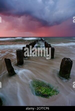 Ein Sturm an der Ostseeküste, raue Meereswellen strömen über das Wellenbrecher am Sandstrand. Stockfoto