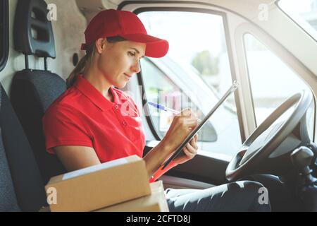 Lieferung Frau in roter Uniform sitzt in van und schriftlich Dokumente Stockfoto