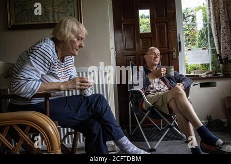 Ältere Paar saß in ihrer Veranda soziale Distanzierung zu Hause während der Coronavirus Pandemie Lockdown, Wales, Vereinigtes Königreich Stockfoto