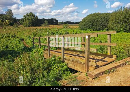 Eine hölzerne Fußgängerbrücke über einen Deich auf einem Canal Walk am ausgedient North Walsham und Dilham Canal in North Walsham, Norfolk, England, Vereinigtes Königreich. Stockfoto