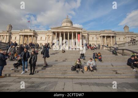 Touristen sahen auf den Stufen vor dem Gebäude der National Gallery am Trafalgar Square in London, Großbritannien, stehen und sitzen. Stockfoto