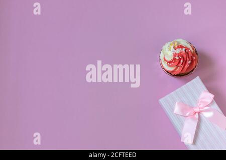 Komposition mit festlichem Cupcake mit rosa Creme und Geschenkbox auf rosa Hintergrund. Tageslicht. Stockfoto