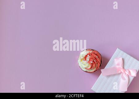 Komposition mit festlichem Cupcake mit rosa Creme und Geschenkbox auf rosa Hintergrund. Tageslicht. Stockfoto