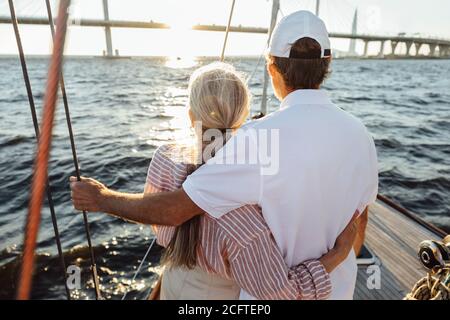 Rückansicht zweier reifer Menschen, die sich umarmen. Seniorenpaar steht auf einem Yachtbogen und schaut in die Ferne. Stockfoto