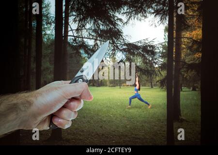 Eine männliche Hand hält ein Messer. Im Hintergrund spielt eine einreisende Frau im Wald Sport. Das Konzept von Kriminalität und Gewalt. Stockfoto