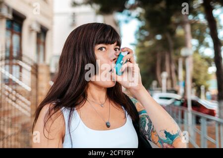 Eine Frau mit einer Tätowierung auf ihrem Arm, die Medizin von einem Inhalator inhaliert. Das Konzept von Asthma. Stockfoto