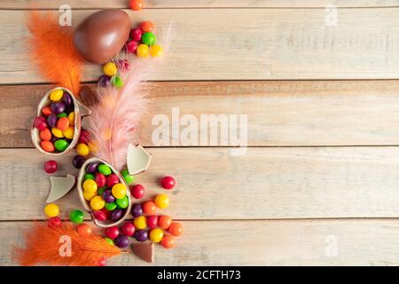 Komposition aus Schokoladeneiern und zarten Federn auf hellem Hintergrund. Bunte Süßigkeiten für den Urlaub. Für Text platzieren. Stockfoto