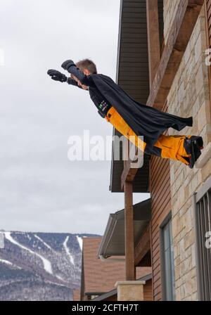 Ein kleiner Junge trägt einen Superhelden Umhang, der von der springt Balkon eines Hauses Stockfoto