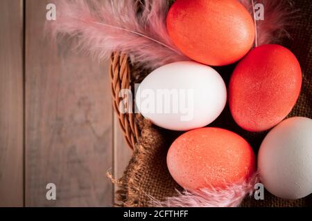 Weiße und orangefarbene ostereier auf hellem Holzhintergrund. Korb mit bunten ostereiern und Federn auf Holzgrund. Rustikaler Stil, Platz für Stockfoto