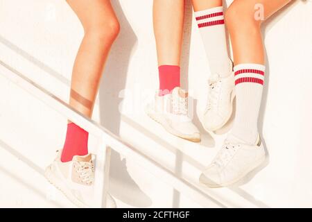 Freundinnen sitzen an der Wand - weiße Sneakers aus nächster Nähe. Sommer sportliche Aktivitäten für Jugendliche, aktive Kinder Lebensstil. Stockfoto