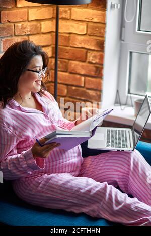 Attraktive schwangere Dame sitzen mit Laptop und Tagebuch, Büroangestellte zu Hause, Schwangerschaft nicht mit der Arbeit stören Stockfoto