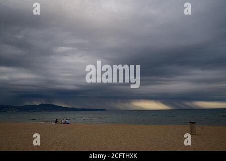 Sant Pere Pescador, Provinz Girona, Spanien. 6. Sep, 2020 - EINE Gruppe von Menschen entspannen sich am Strand von Sant Pere Pescador, Nordspanien, während Regensäulen am Horizont fallen. Das Ende der Sommerferien ist mit stürmischem Wetter gekommen. Quelle: Jordi Boixareu/Alamy Live News Stockfoto