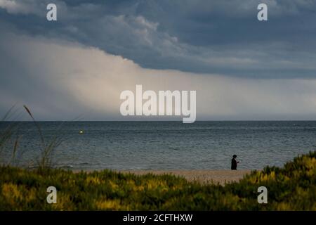 Sant Pere Pescador, Provinz Girona, Spanien. 6. Sep, 2020 - EINE Frau geht am Strand von Sant Pere Pescador, Nordspanien, spazieren, während Regensäulen am Horizont fallen. Das Ende der Sommerferien ist mit stürmischem Wetter gekommen. Quelle: Jordi Boixareu/Alamy Live News Stockfoto