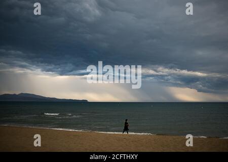 Sant Pere Pescador, Provinz Girona, Spanien. 6. Sep, 2020 - EINE Frau geht am Strand von Sant Pere Pescador, Nordspanien, spazieren, während Regensäulen am Horizont fallen. Das Ende der Sommerferien ist mit stürmischem Wetter gekommen. Quelle: Jordi Boixareu/Alamy Live News Stockfoto