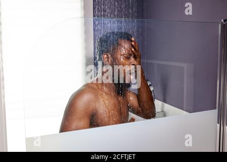 Schwarzer Mann Waschkopf mit Shampoo in der Dusche, genießen Sie das Bad am Morgen. Seitenansicht Stockfoto